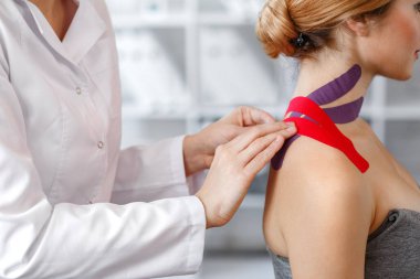 Kineziyoloji bandı. Fizyoterapist hastanın boynuna kinezyoloji bandı uyguluyor. Genç bir atletin yaralı trapezius kaslarını tedavi eden terapist. Travma sonrası rehabilitasyon, spor fizyoterapisi