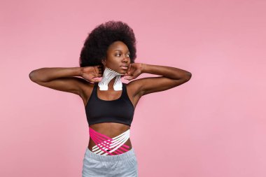 oung smiling female African American athlete on pink background.Kinesiology taping.Kinesiology tape on patient neck, tummy, hip and knee.Sport physical therapy,recovery concept,alternative medicine clipart
