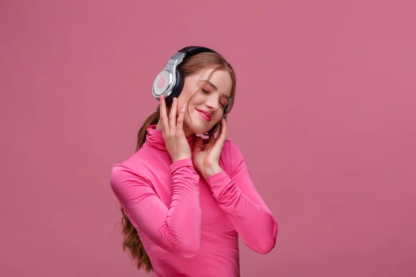 Disfruta escuchando música. Hermosa joven pelirroja en auriculares escuchando música. Chica sonriente divertida en auriculares y blusa rosa bailando sobre fondo rosa. Relajación y manejo del estrés —  Fotos de Stock