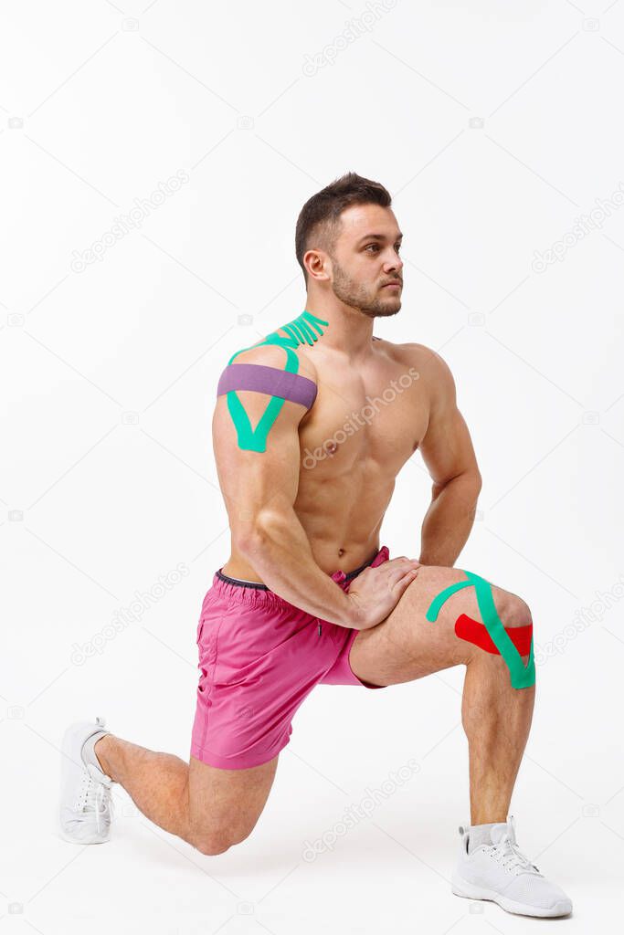 Kinesiology taping. Kinesiology tape on patient knee and shoulder. Young male athlete doing exercises. Post traumatic rehabilitation, sport physical therapy, recovery concept, alternative medicine