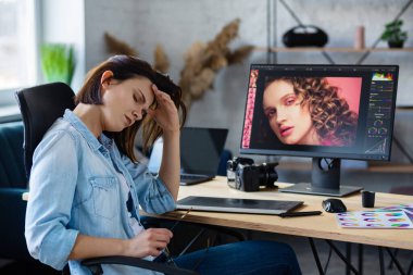 Ofiste fazla mesai yapan yorgun grafik tasarımcısının portresi. Stresli işçilerin göz yorgunluğu belirtileri var. Fotoğraf stüdyosundaki işyerinde. Bitkin ve aşırı çalışma konsepti. Yaratıcı ajans