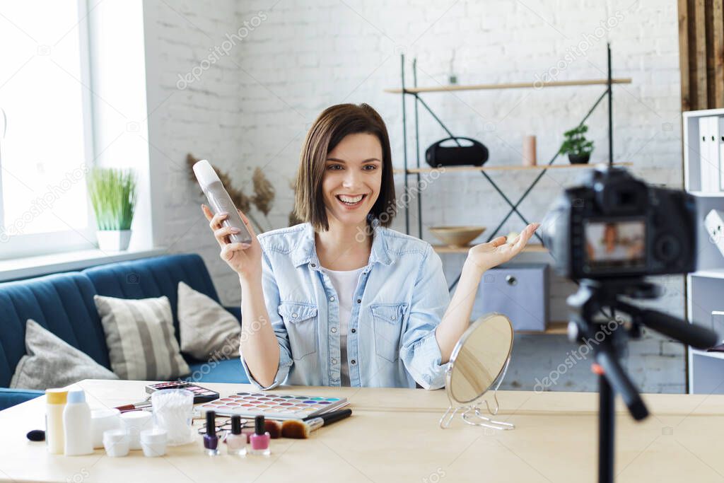 Young female blogger recording a tutorial video for her beauty blog about cosmetics.Vlogger testing hair spray and broadcast live video to social network at home.Blogging, videoblog, makeup concept