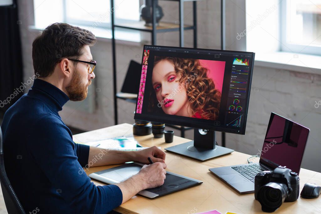 Retouching images in special program.Portrait of graphic designer working in office with laptop,monitor,graphic drawing tablet and color palette.Retoucher workplace in photo studio.Creative agency