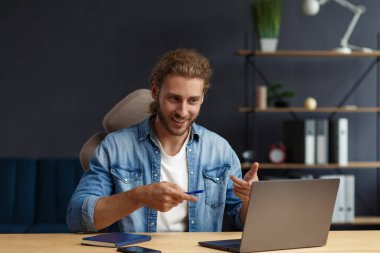 Çevrimiçi, çevrimiçi kurslar. İş kavramı. Uzun saçlı, kıvırcık saçlı, uzun saçlı, evde laptopla çalışan genç, yakışıklı bir müdürün iş portresi.