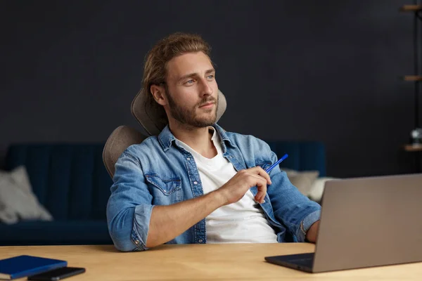 Studying online, online courses. Business concept.Young handsome curly smiling man with long hair studying in home with laptop. Business portrait of handsome manager sitting at workplace