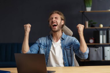 Genç yakışıklı, uzun saçlı, laptopla çalışan ve pozitifliğini ifade eden kıvırcık adam. Mutlu iş adamı olumlu haberler aldı. Ödüllendirildi, yeni sözleşme, iyi anlaşma, başarılı pazarlıklar, en iyi gün.