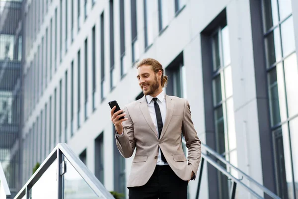 Başarılı genç bir iş adamının portresi. Beyaz tişörtlü, kıvırcık saçlı, telefonu modern bir iş merkezinin arka planında olan bir adam.