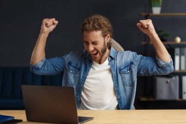 Genç yakışıklı, uzun saçlı, laptopla çalışan ve pozitifliğini ifade eden kıvırcık adam. Mutlu iş adamı olumlu haberler aldı. Ödüllendirildi, yeni sözleşme, iyi anlaşma, başarılı pazarlıklar, en iyi gün.