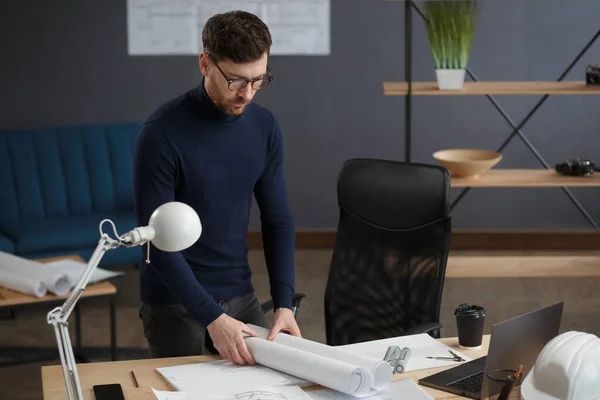 Arquitecto trabajando en la oficina con planos. Ingeniero inspeccionar plan arquitectónico, bosquejando un proyecto de construcción. Retrato de hombre barbudo guapo sentado en el lugar de trabajo. Concepto de construcción empresarial — Foto de Stock