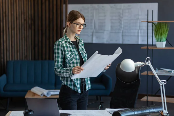 Interieurontwerper werkt in kantoor met blauwdrukken. Ingenieur inspecteert architectuurplan, schets een bouwproject.Portret van mooie vrouw op het werk. Bedrijfsbouwconcept — Stockfoto