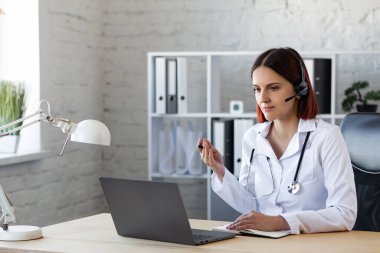 Kadın doktor görüntülü görüşme ile danışmanlık yapıyor. Çevrimiçi tıbbi yardım. Tıp uzmanlarının video konferansı. İş yerindeki bir doktorun portresi. Hasta ve doktor kavramı hakkında konuşuyorlar.