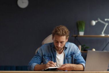 Çevrimiçi, çevrimiçi kurslar. İş kavramı. Uzun saçlı, kıvırcık saçlı, uzun saçlı, evde laptopla çalışan genç, yakışıklı bir müdürün iş portresi.