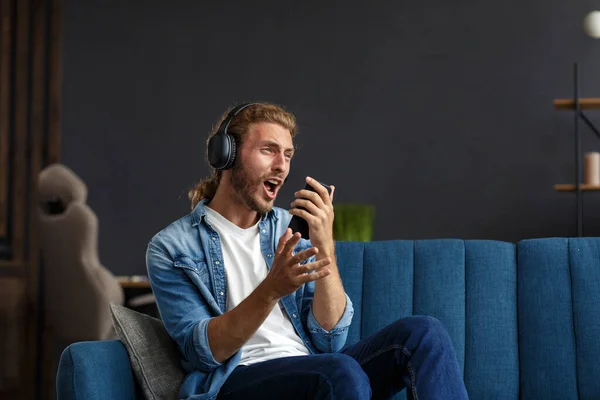 Handsome long haired curly man with headphones listening music,singing and dancing.Funny emotional smiling man with earphones and mobile phone relax at home.Enjoy listening to music.Stress management