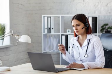 Kadın doktor görüntülü görüşme ile danışmanlık yapıyor. Çevrimiçi tıbbi yardım. Tıp uzmanlarının video konferansı. İş yerindeki bir doktorun portresi. Hasta ve doktor kavramı hakkında konuşuyorlar.