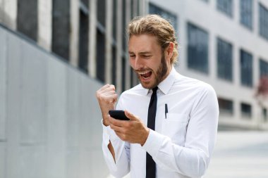 Başarılı genç bir iş adamının portresi. Beyaz tişörtlü, kıvırcık saçlı, telefonu modern bir iş merkezinin arka planında olan bir adam.