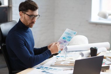 Ofiste renk paletiyle çalışan bir mimar. Mühendis renk örnekleri kullanarak bina için renkler seçiyor, inşaat projesi için yeni fikirler arıyor. İş yerinde sakallı yakışıklı bir adamın portresi.