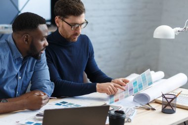Renk paletinde çalışan çok ırklı mühendis takımı. Mimarlar bina renklerini renk örnekleri, çizim ve inşaat projeleri kullanarak seçerler. İş yerinde tartışan ortaklar