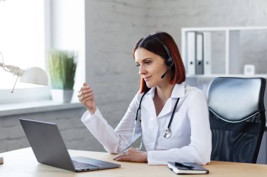 Kadın doktor görüntülü görüşme ile danışmanlık yapıyor. Çevrimiçi tıbbi yardım. Tıp uzmanlarının video konferansı. İş yerindeki bir doktorun portresi. Hasta ve doktor kavramı hakkında konuşuyorlar.
