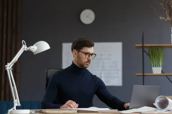 Arquitecto trabajando en la oficina con planos. Ingeniero inspeccionar plan arquitectónico, bosquejando un proyecto de construcción. Retrato de hombre barbudo guapo sentado en el lugar de trabajo. Concepto de construcción empresarial —  Fotos de Stock