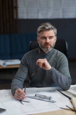 Ofiste planlarla çalışan iç mimar. Mühendis mimari planı inceliyor, bir inşaat projesi çiziyor. İş yerinde sakallı yakışıklı bir adamın portresi. İş inşa kavramı