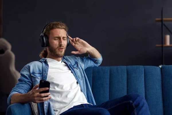 Handsome long haired curly man with headphones listening music,singing and dancing.Funny emotional smiling man with earphones and mobile phone relax at home.Enjoy listening to music.Stress management