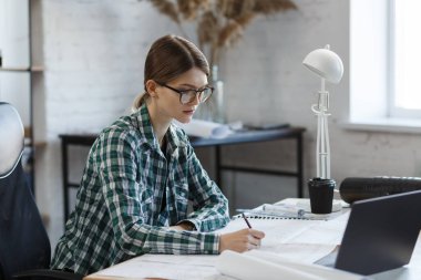 Mimar ofiste planlar çiziyor. Mühendis bir inşaat projesi çiziyor. Mimari plan. İşine odaklanmış güzel bir kadının yakın plan portresi. İş inşa kavramı