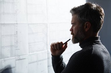 Çalışmaya odaklanmış yakışıklı bir adamın yakın plan portresi. Ofiste planlarla çalışan bir mimar. Mühendis bir inşaat projesi çiziyor. Mimari plan. İş inşa kavramı