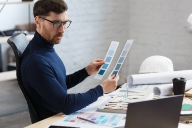 Ofiste renk paletiyle çalışan bir mimar. Mühendis renk örnekleri kullanarak bina için renkler seçiyor, inşaat projesi için yeni fikirler arıyor. İş yerinde sakallı yakışıklı bir adamın portresi.