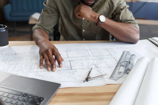 Arquitecto afro-americano que trabaja en oficina con planos. Ingeniero inspecciona plano arquitectónico, dibujando un proyecto de construcción. Retrato de un hombre guapo negro sentado en el lugar de trabajo. Concepto empresarial — Foto de Stock