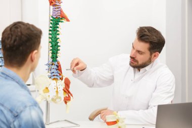 Doktor, hastasına esnek omurga modeli gösteriyor ve muayenehanedeki ağrısının nedenini açıklıyor. Klinikteki fizyoterapisti ziyaret eden hasta. Cerrahi, sağlık ve tıp konsepti