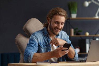 Genç adam akıllı telefon kullanıyor ve gülümsüyor. Mutlu iş adamı cep telefonu uygulamaları kullanıyor, mesaj atıyor, internette geziniyor, akıllı telefona bakıyor. Mobil aygıtlarla çalışan gençlerin kavramı