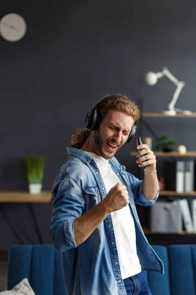 Handsome long haired curly man with headphones listening music,singing and dancing.Funny emotional smiling man with earphones and mobile phone relax at home.Enjoy listening to music.Stress management