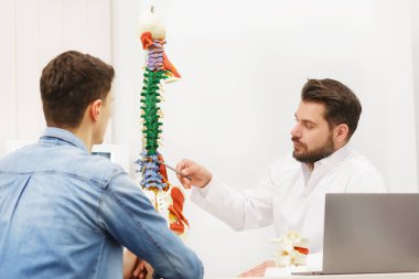 Doktor, hastasına esnek omurga modeli gösteriyor ve muayenehanedeki ağrısının nedenini açıklıyor. Klinikteki fizyoterapisti ziyaret eden hasta. Cerrahi, sağlık ve tıp konsepti