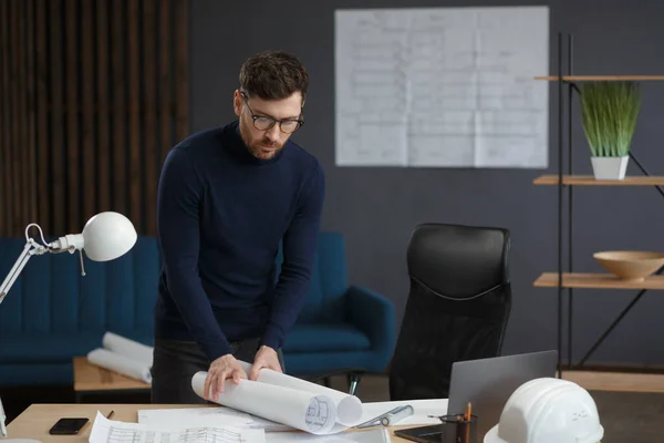 Arquitecto trabajando en la oficina con planos. Ingeniero inspeccionar plan arquitectónico, bosquejando un proyecto de construcción. Retrato de hombre barbudo guapo sentado en el lugar de trabajo. Concepto de construcción empresarial — Foto de Stock