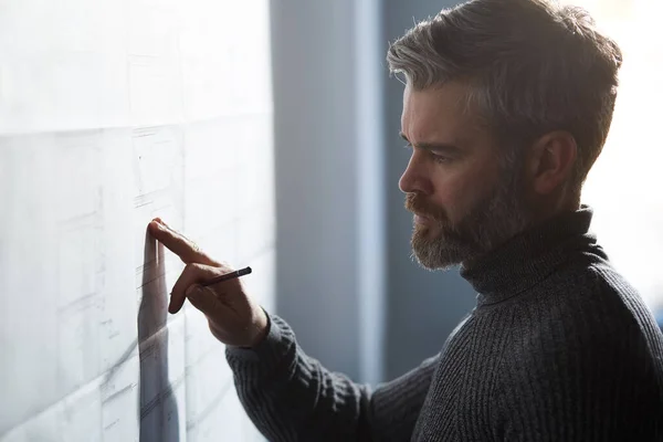 Retrato de cerca del hombre guapo concentrado en el trabajo. Arquitecto trabajando en oficina con planos. Ingeniero dibujando un proyecto de construcción. Plano arquitectónico. Concepto de construcción empresarial —  Fotos de Stock