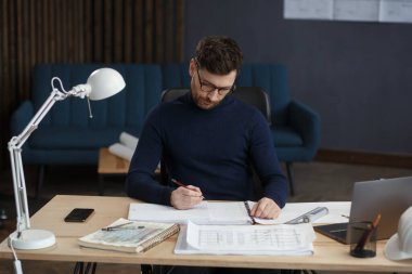 Ofiste planlarla çalışan bir mimar. Mühendis mimari planı inceliyor, bir inşaat projesi çiziyor. İş yerinde oturan sakallı yakışıklı bir adamın portresi. İş inşa kavramı