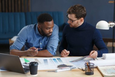 Renk paletinde çalışan çok ırklı mühendis takımı. Mimarlar bina renklerini renk örnekleri, çizim ve inşaat projeleri kullanarak seçerler. İş yerinde tartışan ortaklar