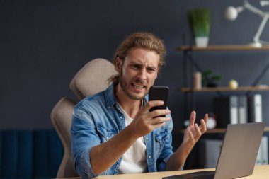 Dizüstü bilgisayar kullanan sinirli, genç, kıvırcık adam. Stresli serbest çalışan biri, çalışmayan dizüstü bilgisayarında veri kaybetmiş. Kötü haber ya da e-posta alınıyor, spam mesajı. Mobil aygıtlarla çalışan gençler