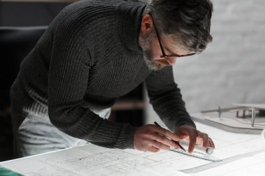 Mimar ofiste planlar çiziyor. Mühendis bir inşaat projesi çiziyor. Mimari plan. Yakışıklı sakallı adamın işine odaklanmış yakın plan portresi. İş inşa kavramı