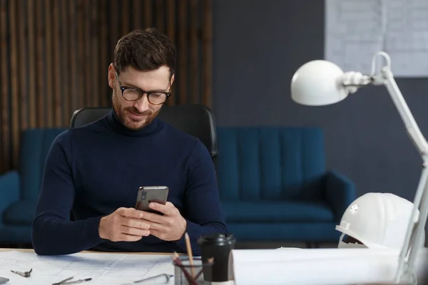 Jovem usando smartphone e sorrindo. Empresário feliz usando aplicativos de telefone celular, mensagem de texto, navegando na internet, olhando para o smartphone. Conceito de jovens que trabalham com dispositivos móveis — Fotografia de Stock