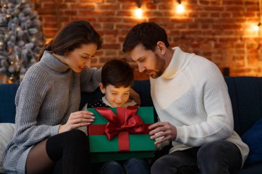 Anne babalar sevimli oğluna hediye paketi sunuyor. Noel çocukları, çocuk, portre. Mutlu bir aile Noel sabahı birlikte geçirir. Kış tatilleri, Noel kutlamaları, yeni yıl konsepti.