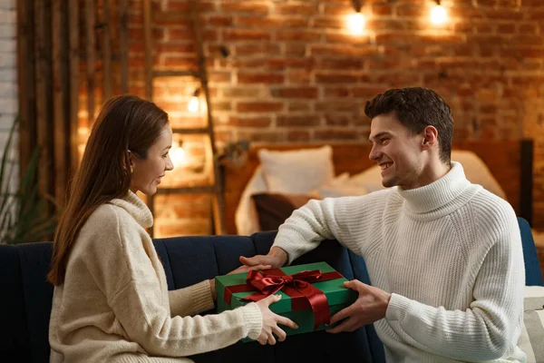 Красивый мужчина преподносит подарок своей красивой девушке и улыбается. Прекрасная молодая пара дома наслаждается проведением времени вместе. Зимние праздники, рождественские праздники, новогодняя концепция — стоковое фото