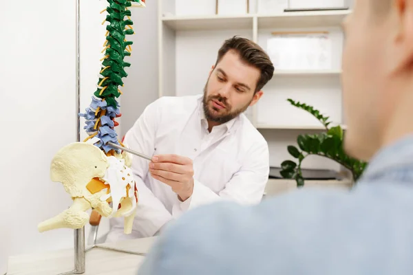Lekarz pokazuje pacjentowi elastyczny model kręgosłupa i wyjaśnia przyczynę bólu w gabinecie medycznym. Pacjent odwiedzający fizjoterapeutę w klinice. Koncepcja chirurgii, opieki zdrowotnej i medycyny — Zdjęcie stockowe