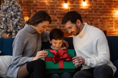 Anne babalar sevimli oğluna hediye paketi sunuyor. Noel çocukları, çocuk, portre. Mutlu bir aile Noel sabahı birlikte geçirir. Kış tatilleri, Noel kutlamaları, yeni yıl konsepti.