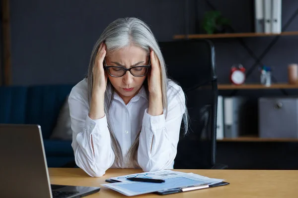 Burnout and overwork concept.Fáradt üzletasszony túlórázik.Portré a stresszes ősz hajú idős nő fejfájással.Szemfeszülés munka után a laptop.Vállalkozó csődbe — Stock Fotó