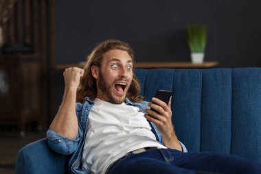 Kıvırcık saçlı bir adam, cep telefonundan harika haberler izliyor. SMS mesajları alan öğrenci iyi haberler okuyor. Apartmanda zaferi kutlayan şaşırmış adam.