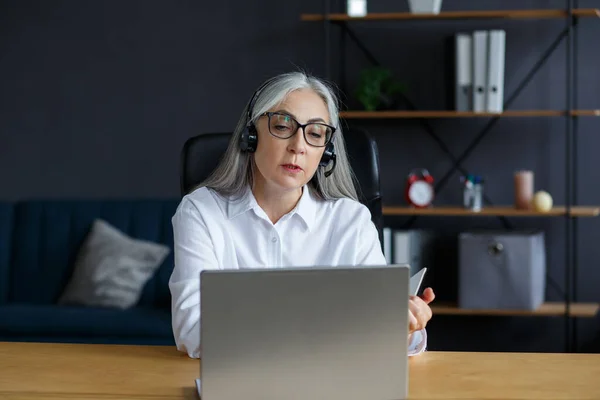 Retrato de bela mulher idosa sorridente estudando online. Educação on-line, trabalho remoto, educação em casa. Mulher de cabelos grisalhos a escrever no caderno. Pessoas maduras estudam cursos online — Fotografia de Stock