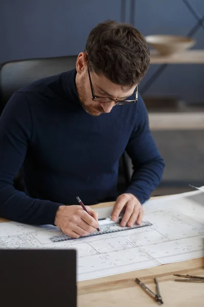 Arquitecto trabajando en la oficina con planos. Ingeniero inspeccionar plan arquitectónico, bosquejando un proyecto de construcción. Retrato de hombre barbudo guapo sentado en el lugar de trabajo. Concepto de construcción empresarial — Foto de Stock