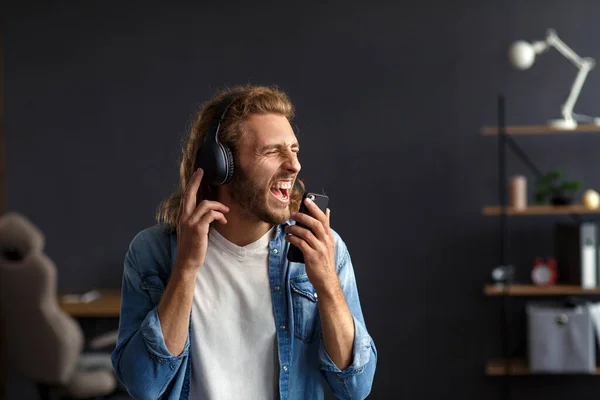 Handsome long haired curly man with headphones listening music,singing and dancing.Funny emotional smiling man with earphones and mobile phone relax at home.Enjoy listening to music.Stress management