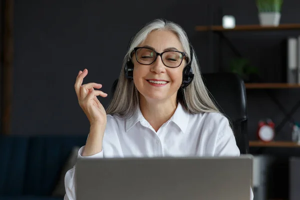 Retrato de una mujer madura de pelo gris sonriente usando un portátil para una reunión en línea, videollamada, videoconferencia. Comunicación en línea con colegas o familiares. Educación en línea, trabajo a distancia —  Fotos de Stock